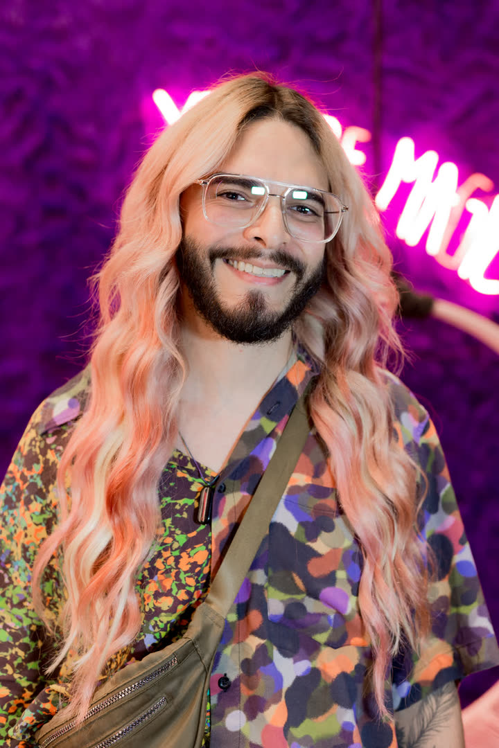 Cliente MOJO de cabelo longo diante do letreiro de neon YOU ARE MAGIC